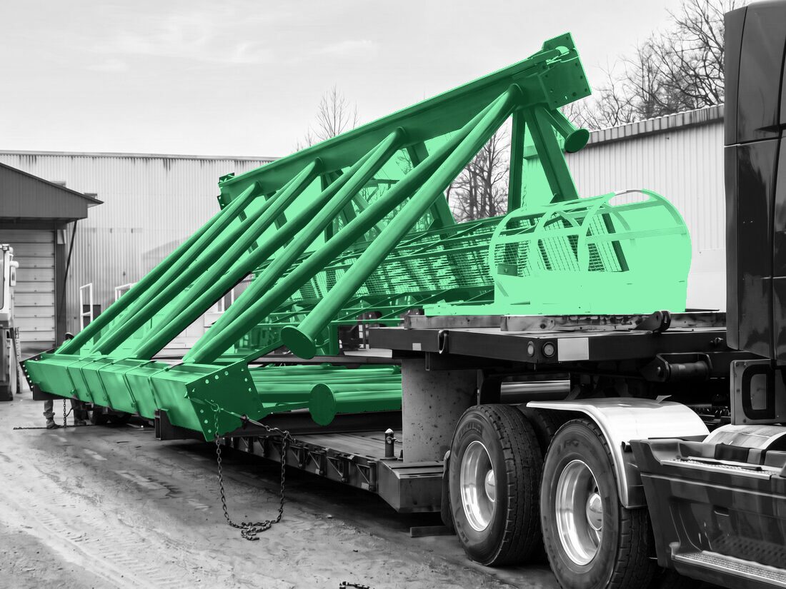 Red lattice mast (drill rig / pile-driver boom) with operator cage on low-bed trailer