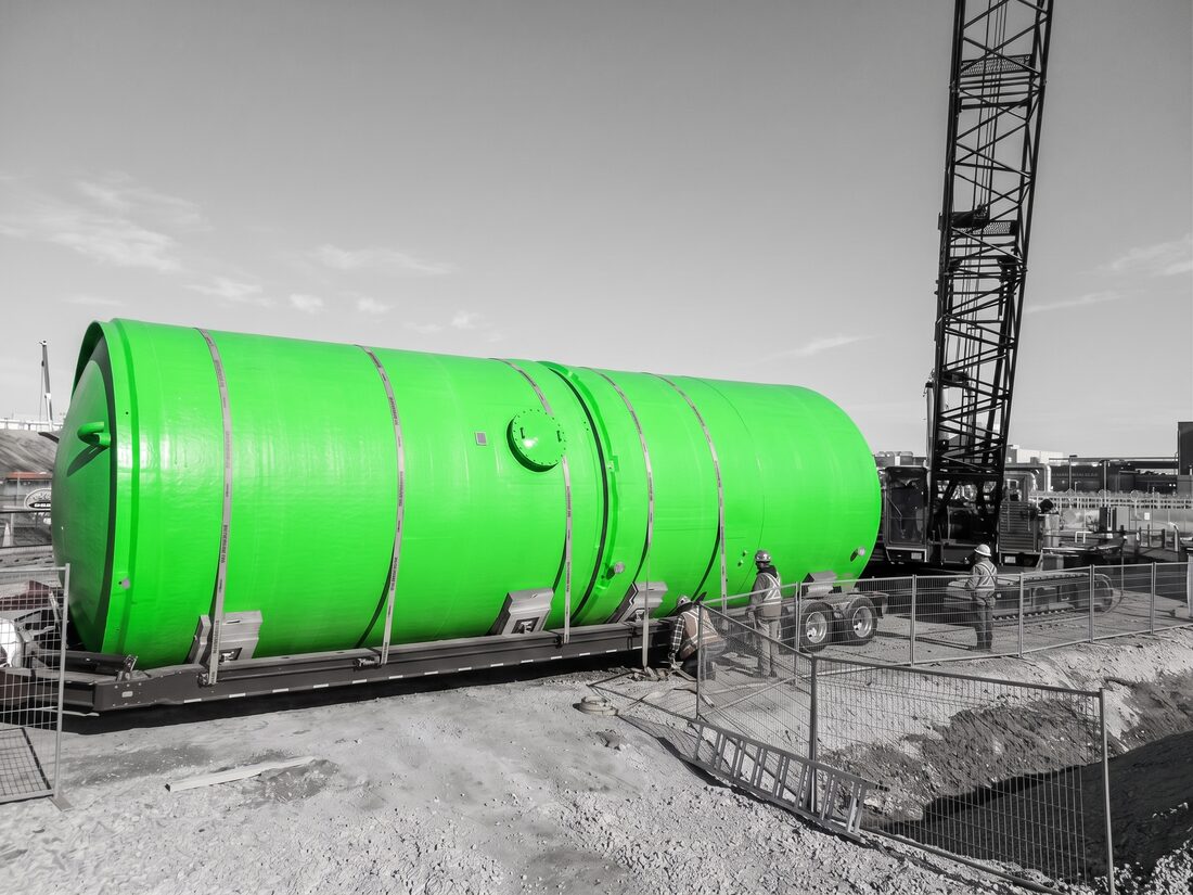 Large cylindrical chemical process tank on low-bed trailer being delivered to construction site