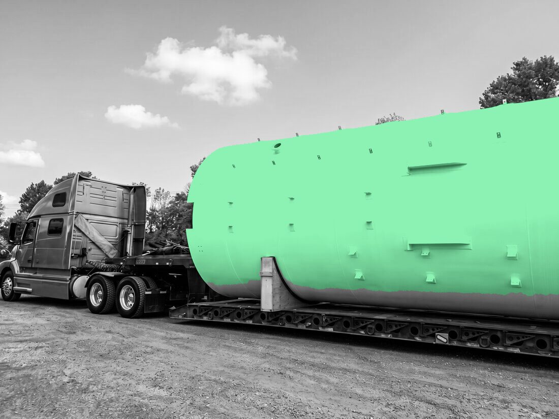 Large white fiberglass storage tank on lowboy pulled by blue Volvo