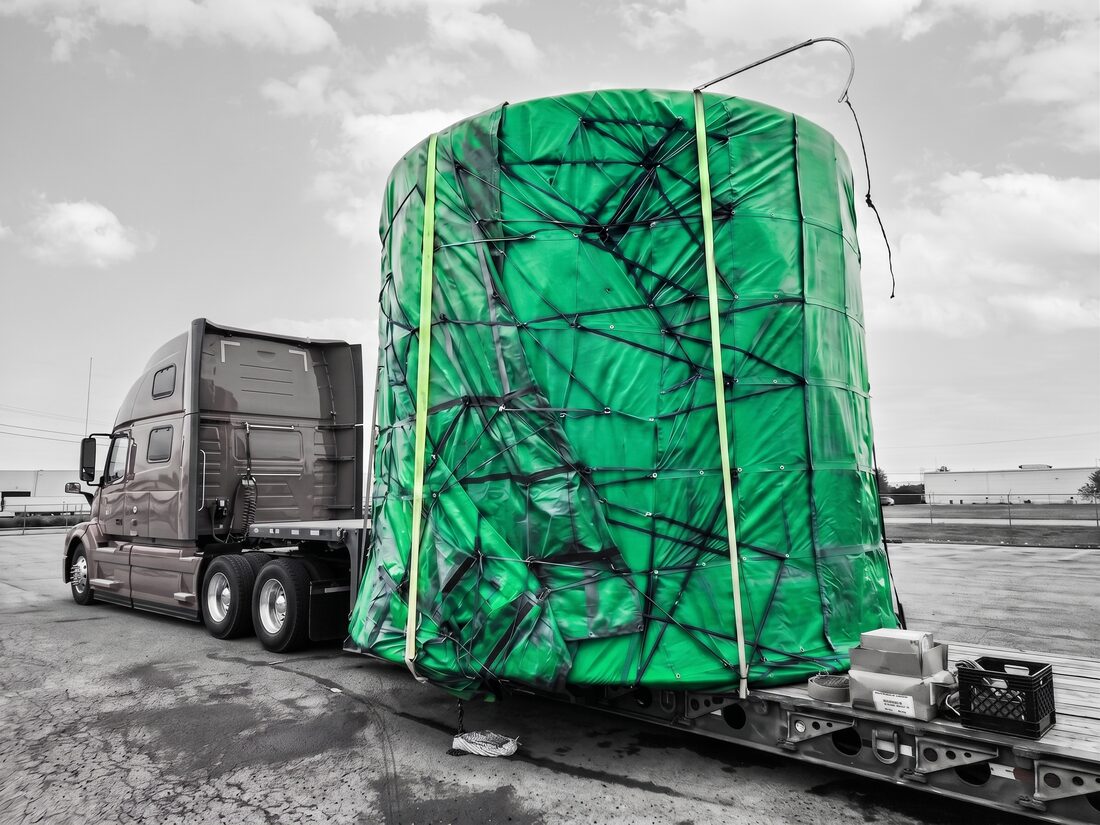 Same large blue-tarp-wrapped industrial tank on lowboy — closer side view