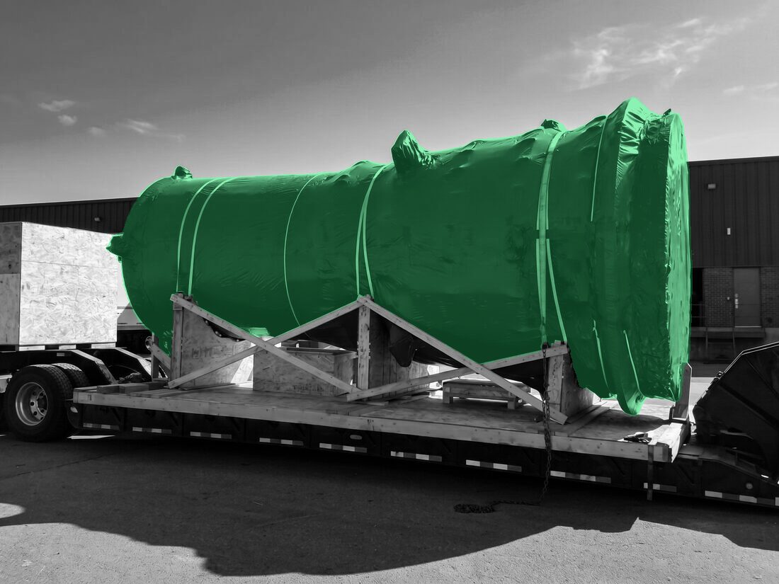 Blue-tarped industrial cyclone separator / process vessel on wood skid on step-deck flatbed