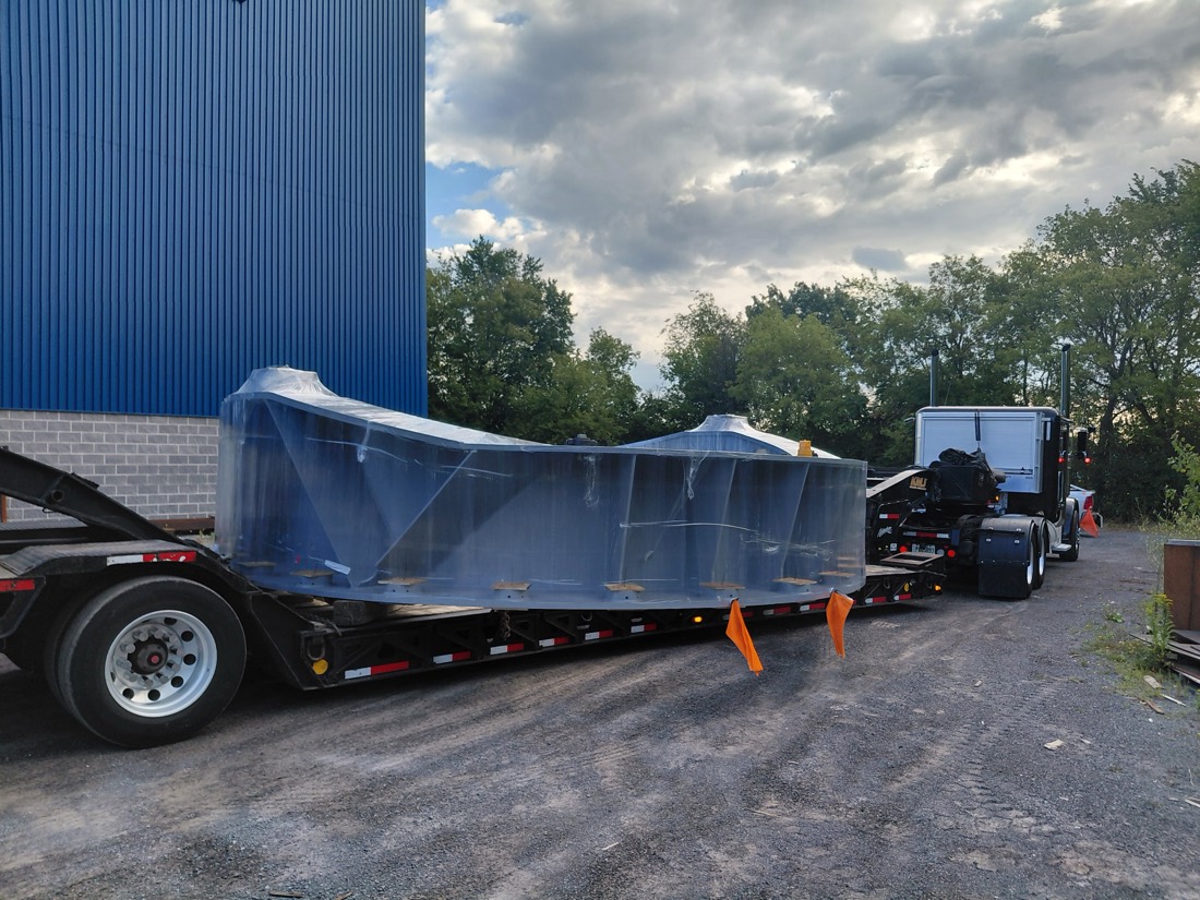 Large fabricated steel structure (machine frame / chassis) wrapped in protective film on step-deck