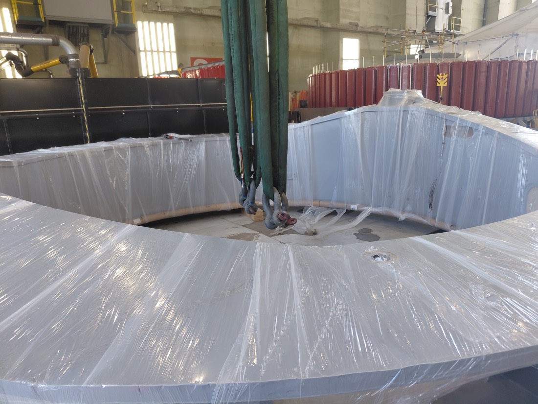 Large steel ring / mill or TBM shell section in plastic wrap, lifted by overhead crane inside fabrication shop