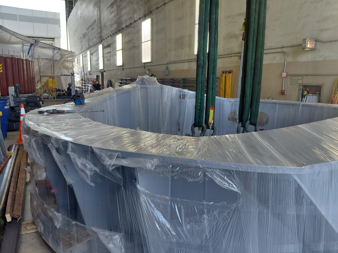 Closer view of same large steel ring / shell section in plastic wrap with overhead crane slings