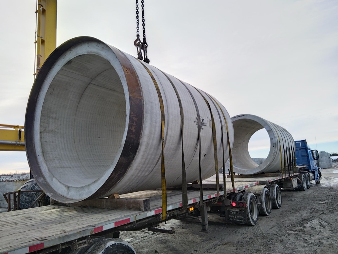 Precast concrete culvert / pipe sections being loaded on flatbed by yellow gantry crane