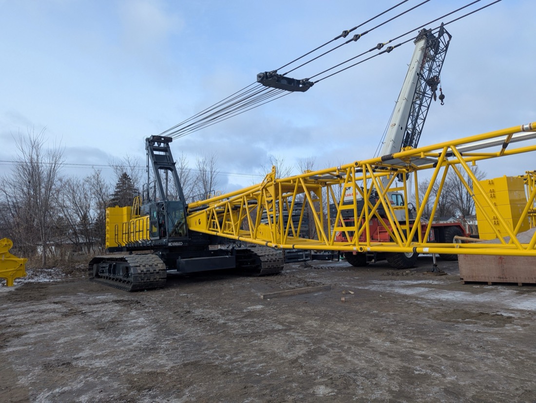 Kobelco lattice-boom crawler crane being assembled with boom sections and counterweights staged on ground