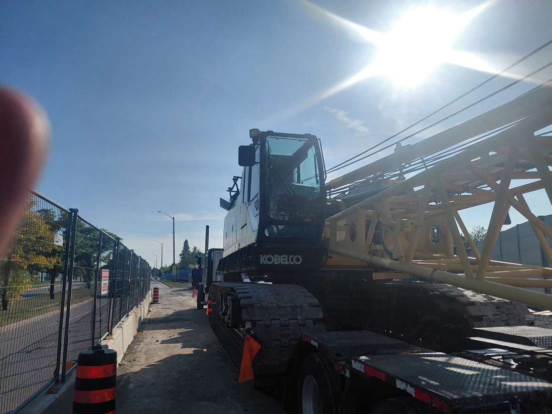 Kobelco crawler crane loaded on low-bed trailer at street-side job site