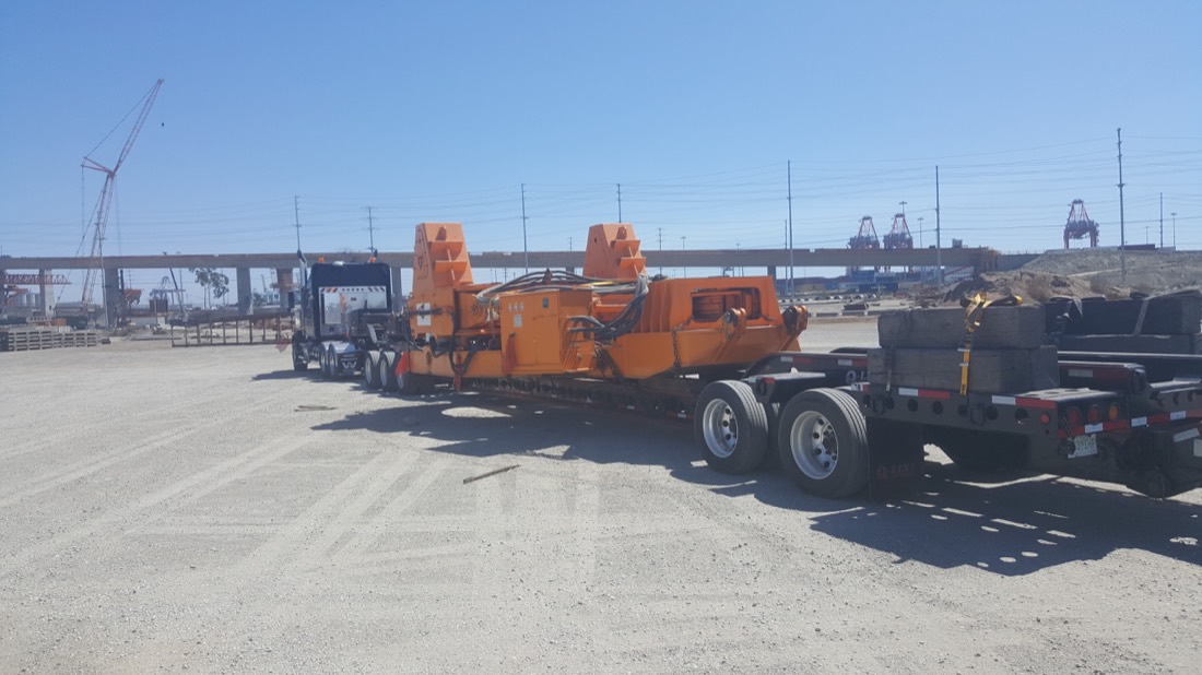 Orange horizontal directional drilling (HDD) rig / pipe-handling equipment on low-bed trailer at port