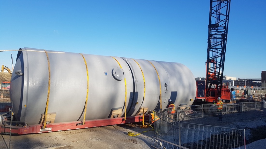 Large cylindrical chemical process tank on low-bed trailer being delivered to construction site