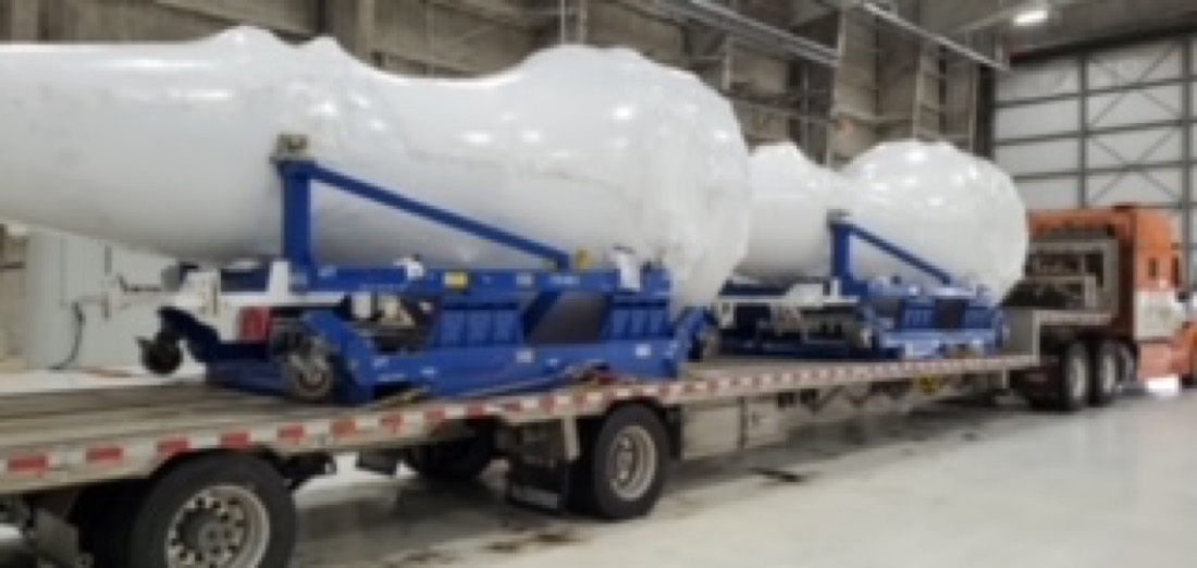 Two large white cylindrical pressure vessels / storage tanks on blue cradles on step-deck flatbed