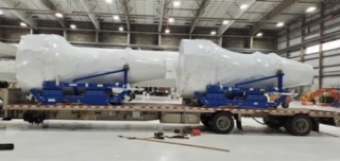 Same two white pressure vessels on blue cradles on flatbed — side view in warehouse