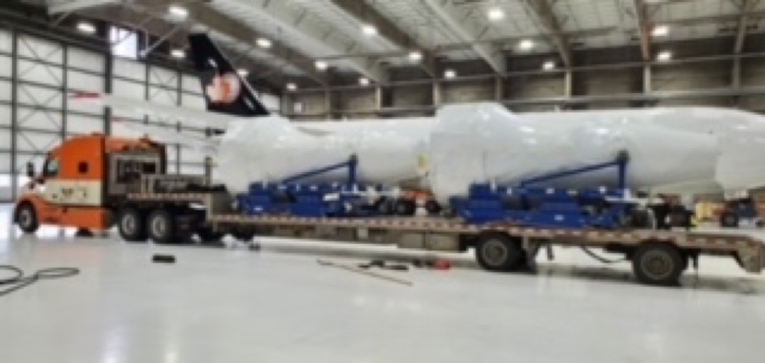 Same pressure vessels with orange Mack tractor hooked to step-deck — wider warehouse view