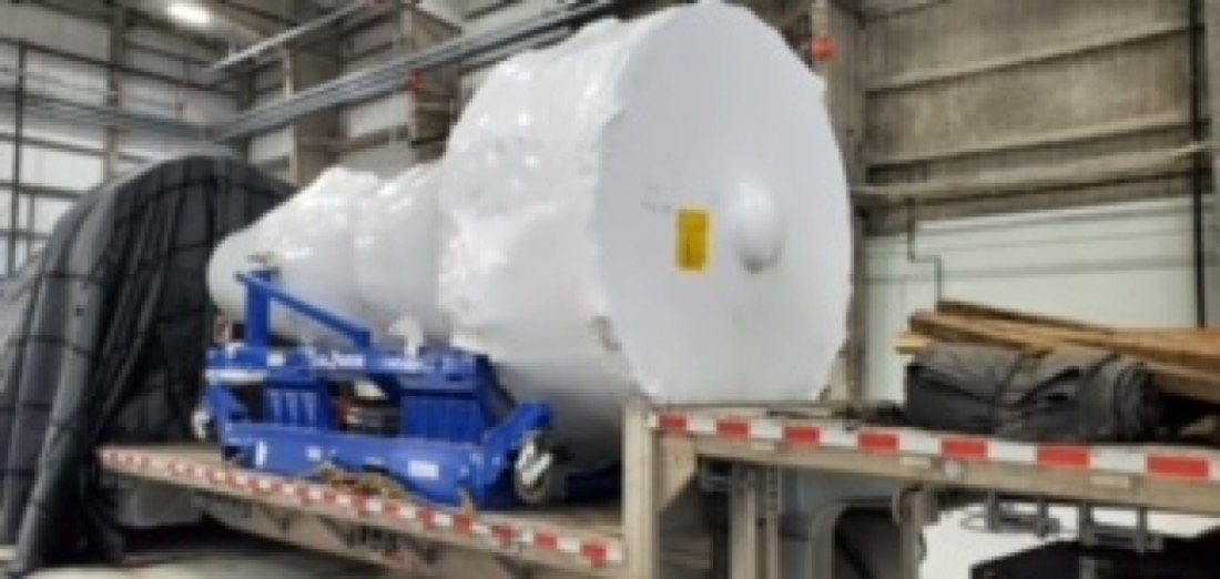 Close-up of white shrink-wrapped pressure vessels on blue cradles, step-deck flatbed