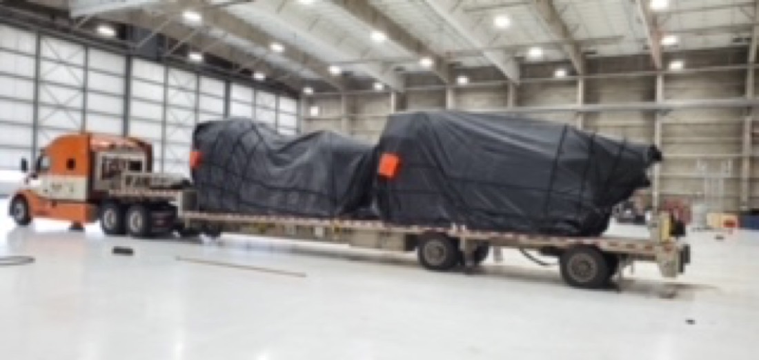 Same tarped aircraft components with orange Mack tractor hooked up — wider view