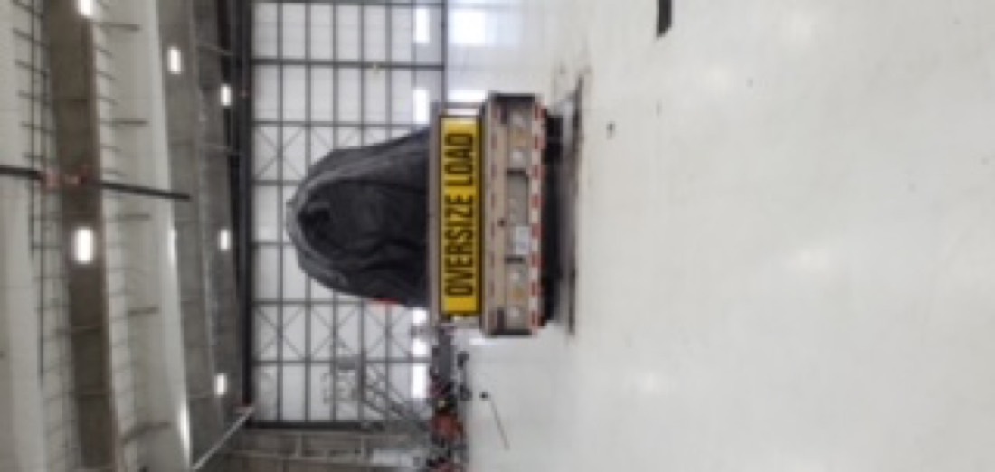Rear view of tarped oversize cargo on flatbed with OVERSIZE LOAD banners