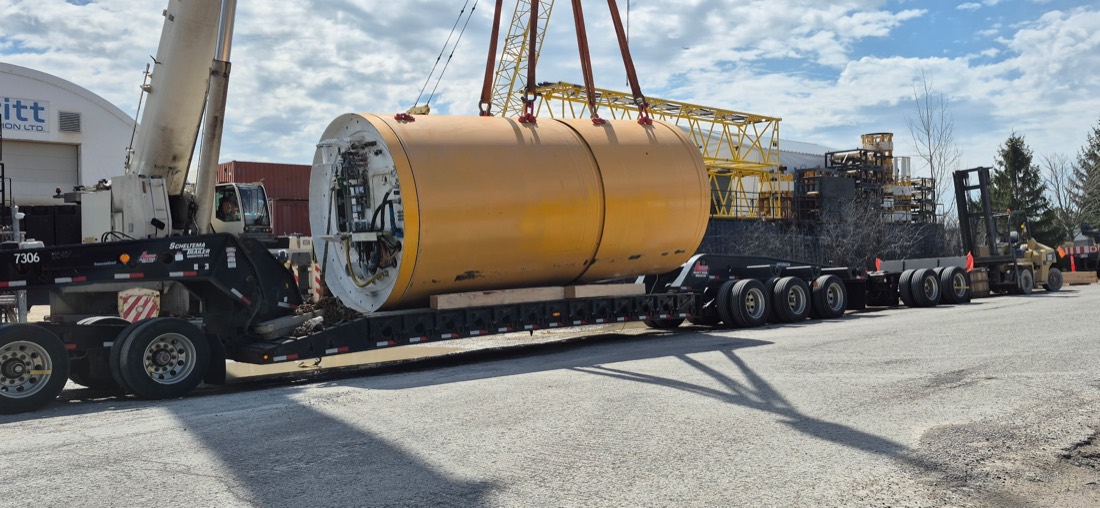 Massive yellow TBM shield / industrial drum being lowered onto Scheuerle modular trailer by mobile crane