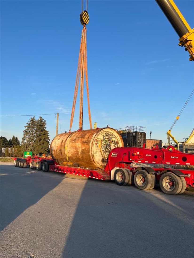 Rusty TBM trailing shield / rotary drum being lifted onto red Aspen NXT modular trailer by mobile crane