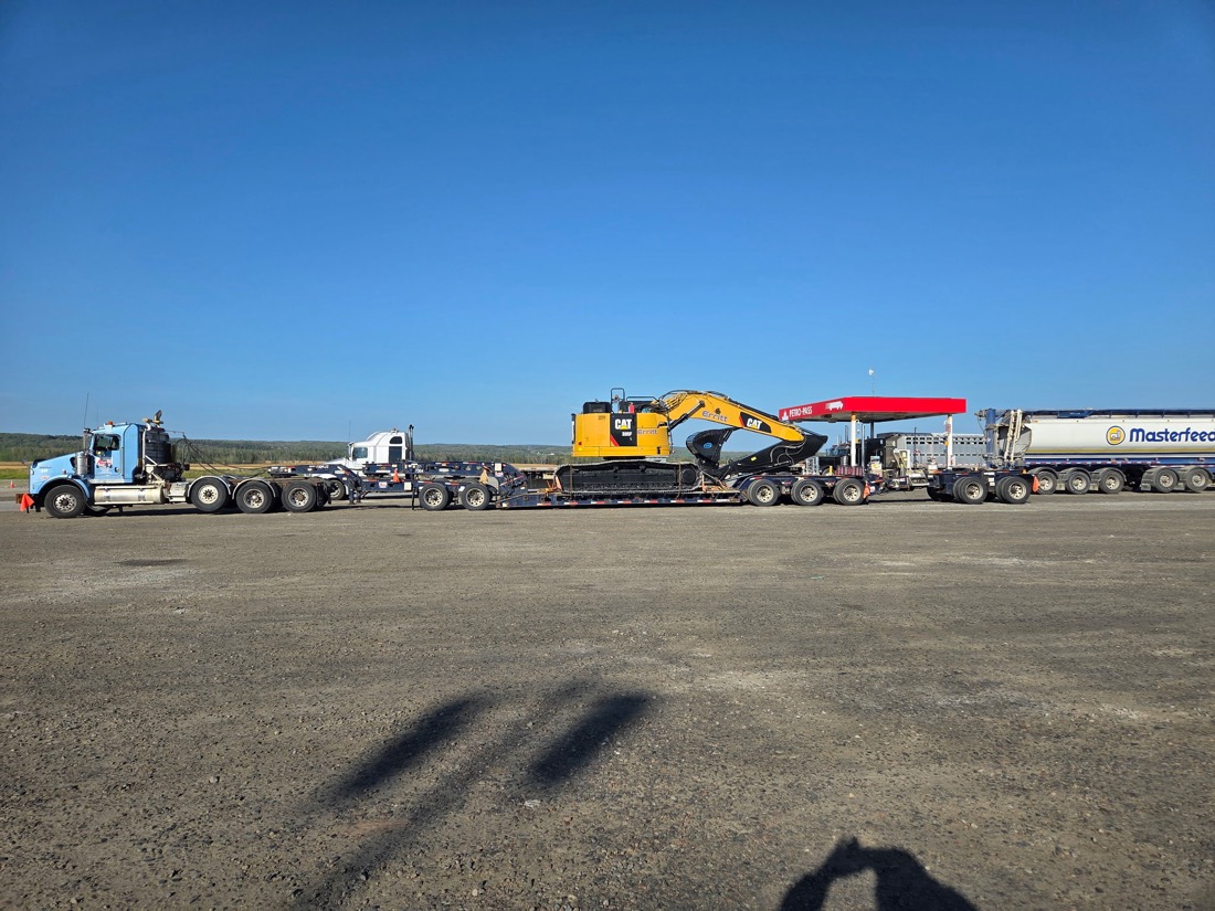 Cat hydraulic excavator on lowboy with blue tractor at fuel stop