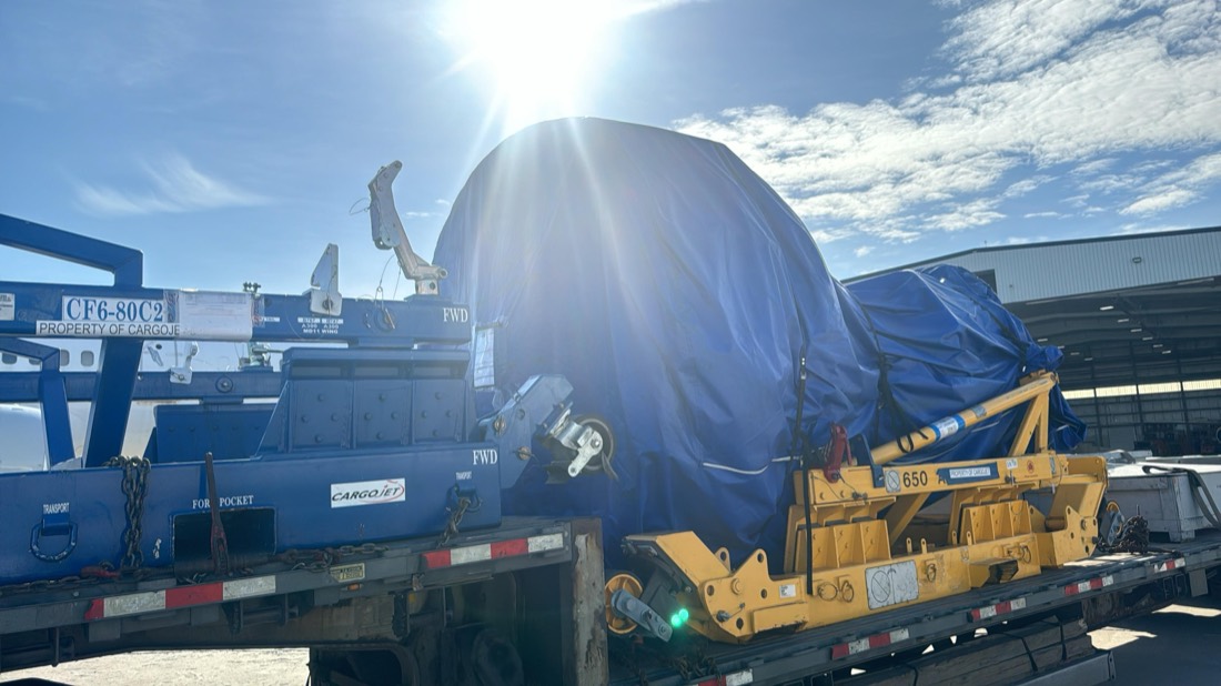 GE CF6-80C2 jet engine (Cargojet) on blue transport stand, tarp-covered on flatbed