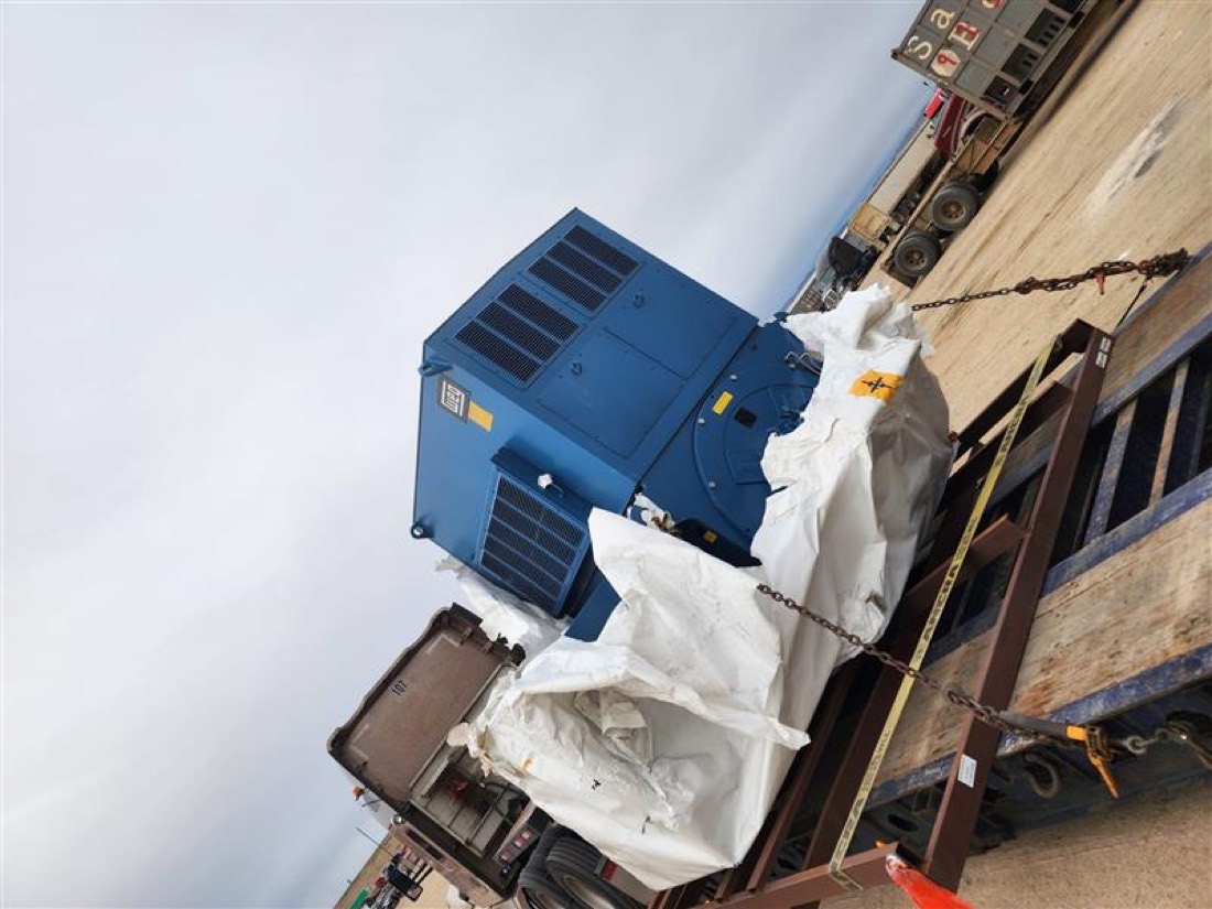 Large blue industrial electric motor / generator chain-secured on flatbed trailer