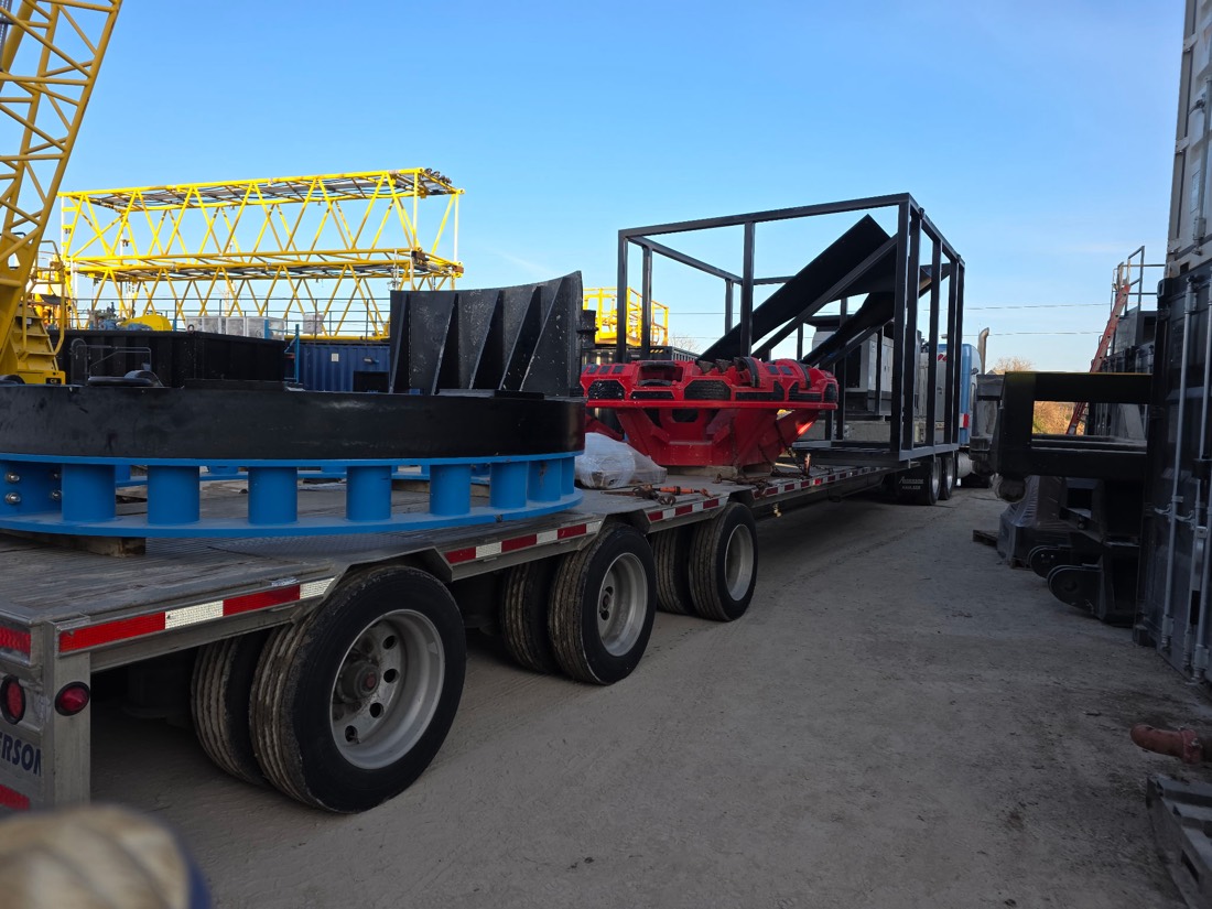 Mining mill discharge head, blue base, red impeller in transport frames; yellow crane boom in background