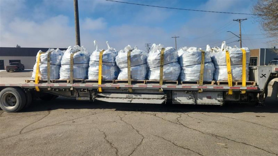 Rows of white bulk bags / super sacks (FIBC) on pallets, strap-secured on flatbed