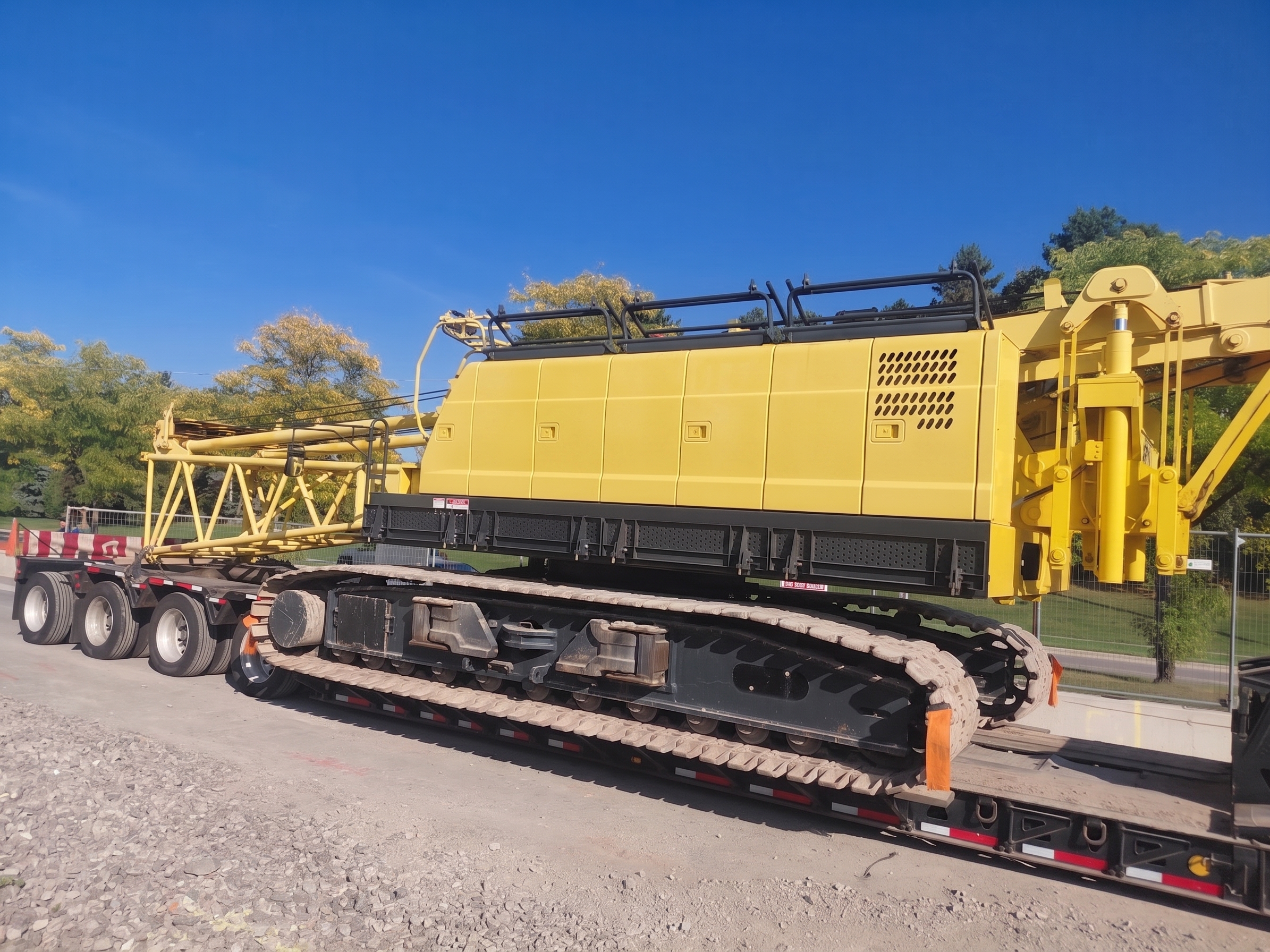 Yellow crawler crane on multi-axle lowboy; lattice booms on adjacent trailer