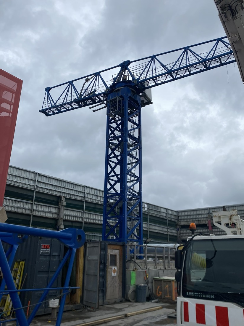 Blue tower crane being erected at construction site, Liebherr mobile crane assisting