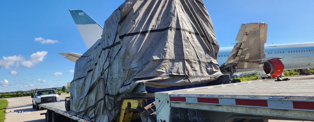 Tarp-wrapped aircraft engine on stand on flatbed at airport (Cargojet aircraft behind)