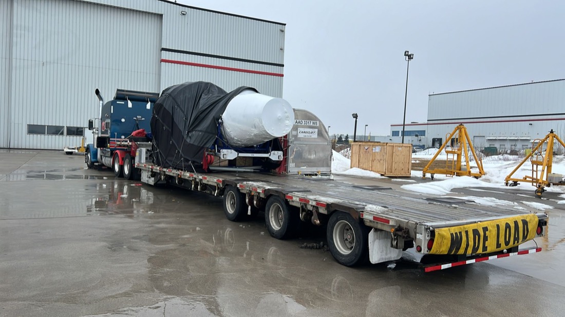 Blue Peterbilt with Cargojet CF6-80C2 jet engine on blue stand, partially tarped, on WIDE LOAD step-deck