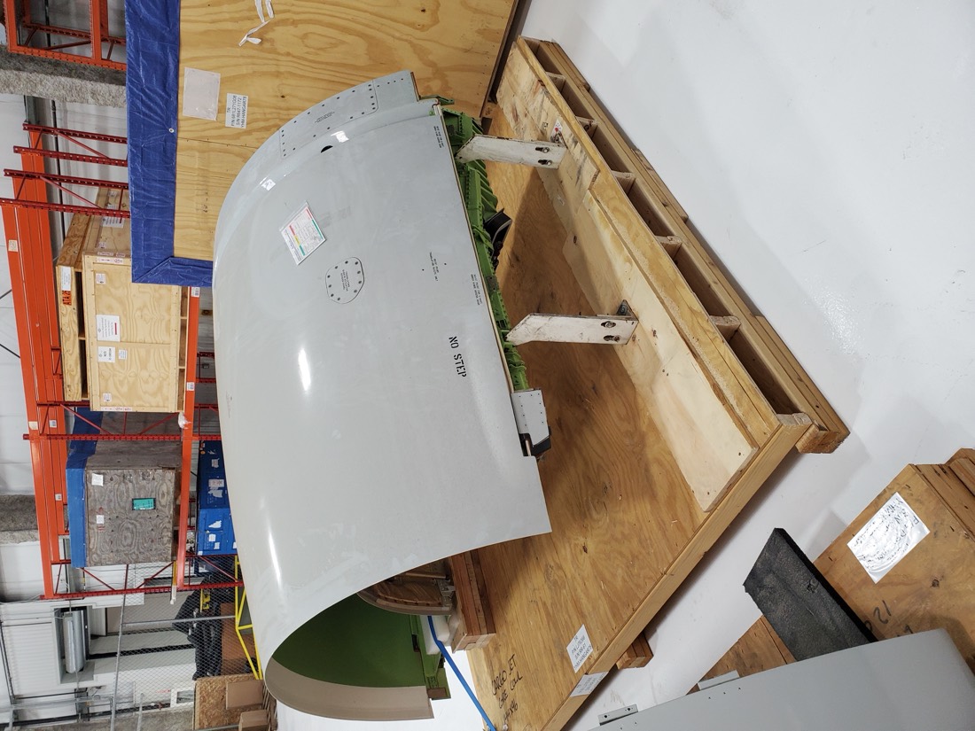 Aircraft engine cowling / nacelle (white "NO STEP") on wood shipping crate in aerospace warehouse