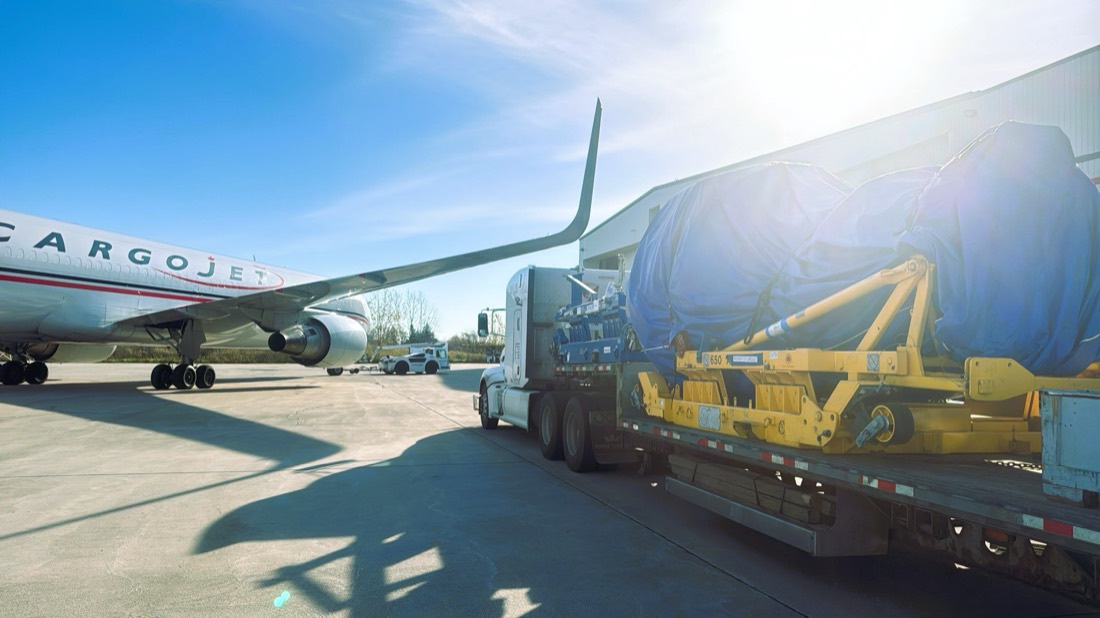 Cargojet jet engine on yellow stand, tarp-covered, on flatbed alongside parked Cargojet 757/767