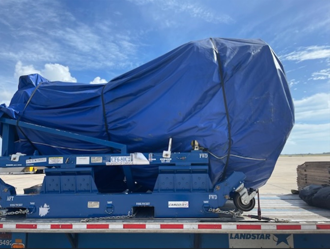 Blue-tarp-wrapped CF6 jet engine on stand on flatbed — interstate transit