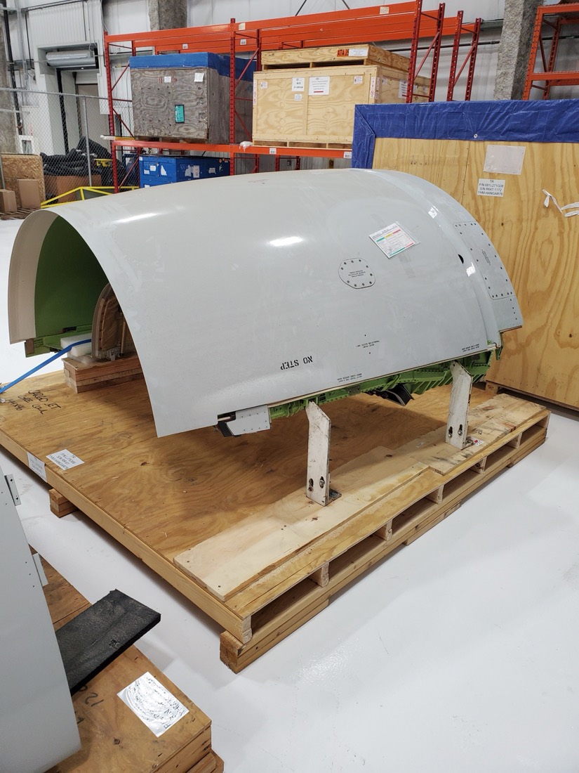 Aircraft engine cowling / thrust-reverser nacelle on wooden shipping pallet in aerospace warehouse