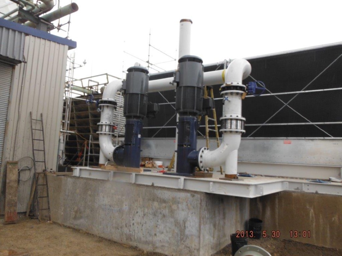 Two large vertical-shaft cooling-water pumps with motors installed beside cooling tower