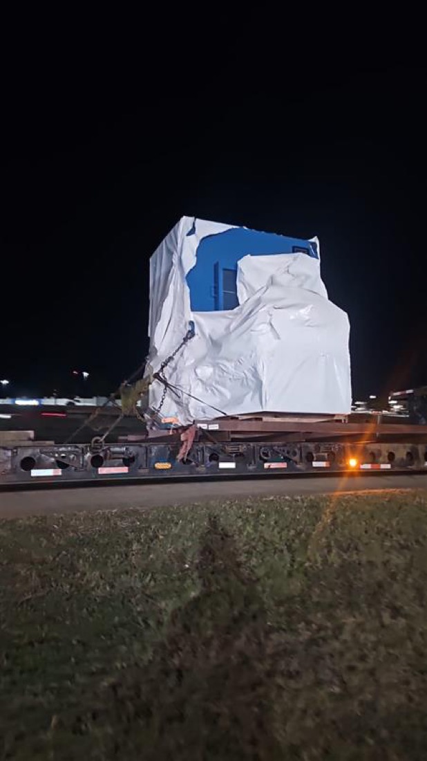 Tarp-wrapped industrial machinery (electrical cabinet / generator) on lowboy trailer at night