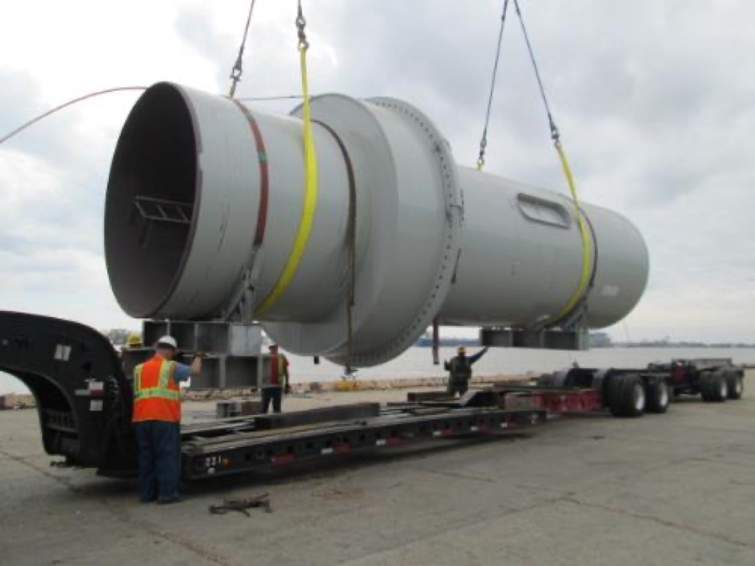 Large gray cylindrical industrial vessel / SCR module being loaded on extendible double-drop with jeep at port