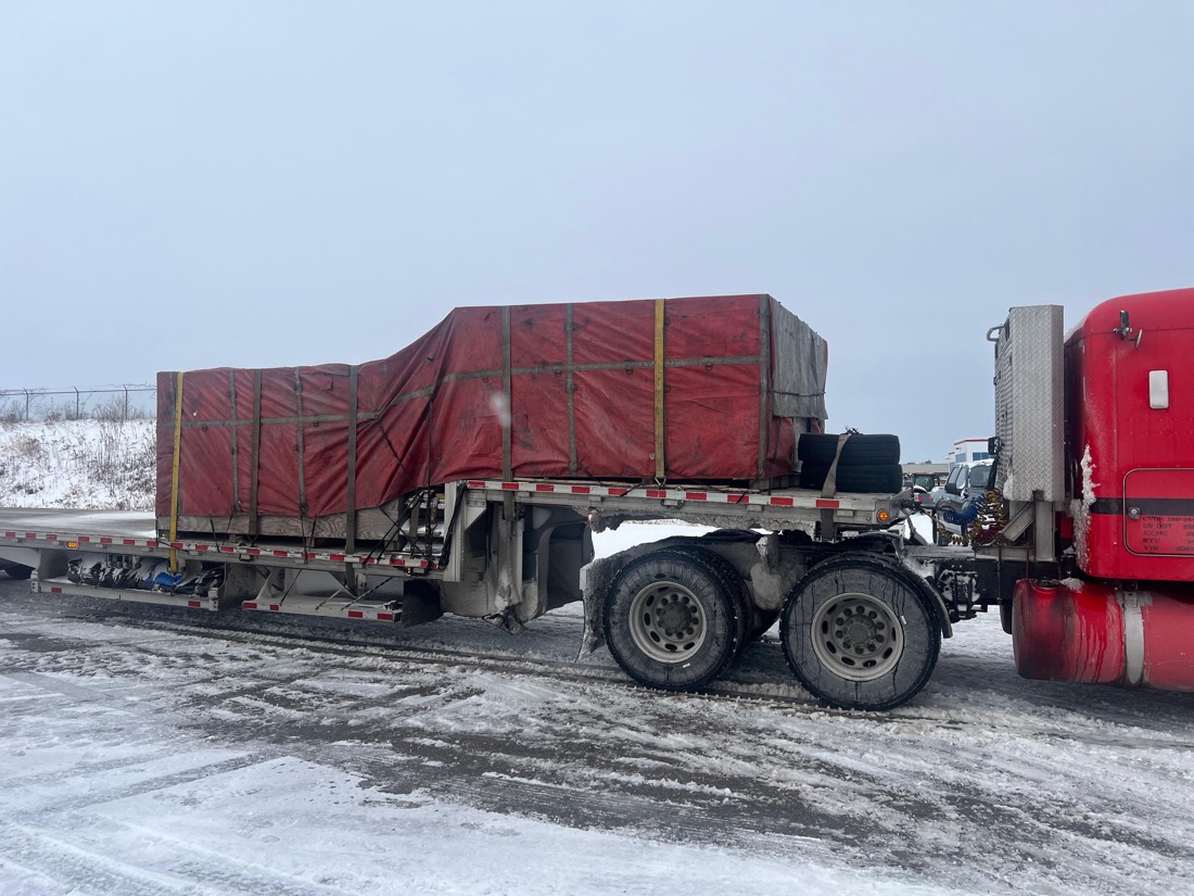 Red-tarped cargo with aircraft tires on step-deck flatbed in winter
