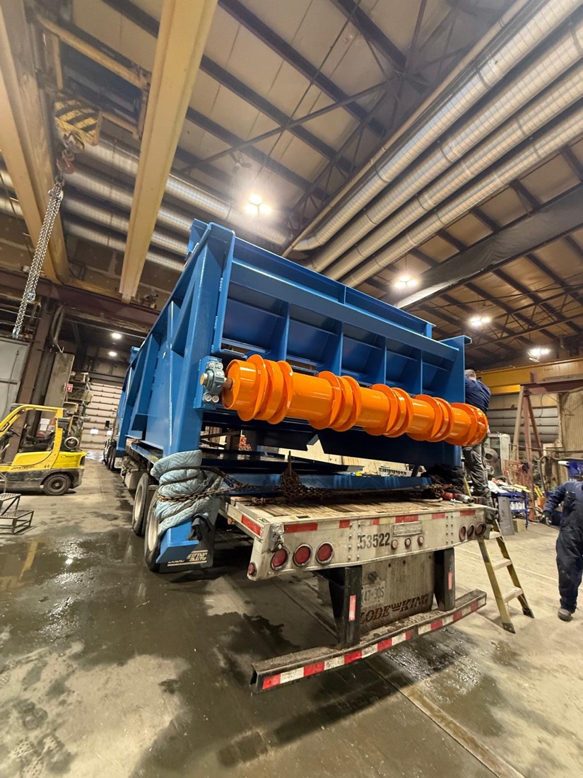 Blue housing with orange toothed roller (mining roll crusher / sizer) on flatbed in warehouse