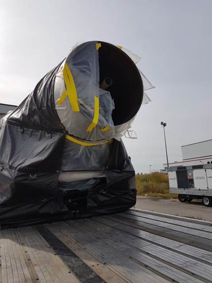 Large tarp-wrapped industrial cylindrical vessel / pipe section on step-deck flatbed
