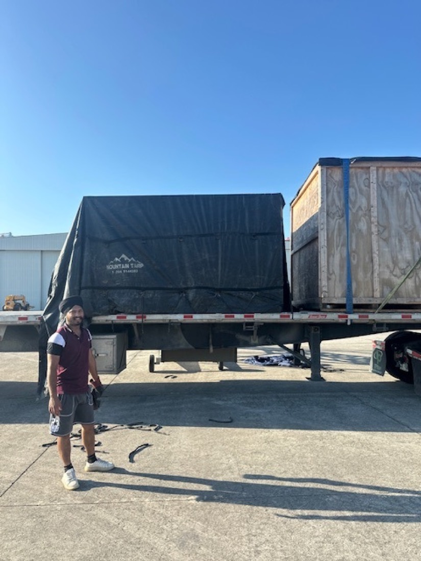 Driver standing beside flatbed with Mountain Tarp wrapped cargo and wooden crate