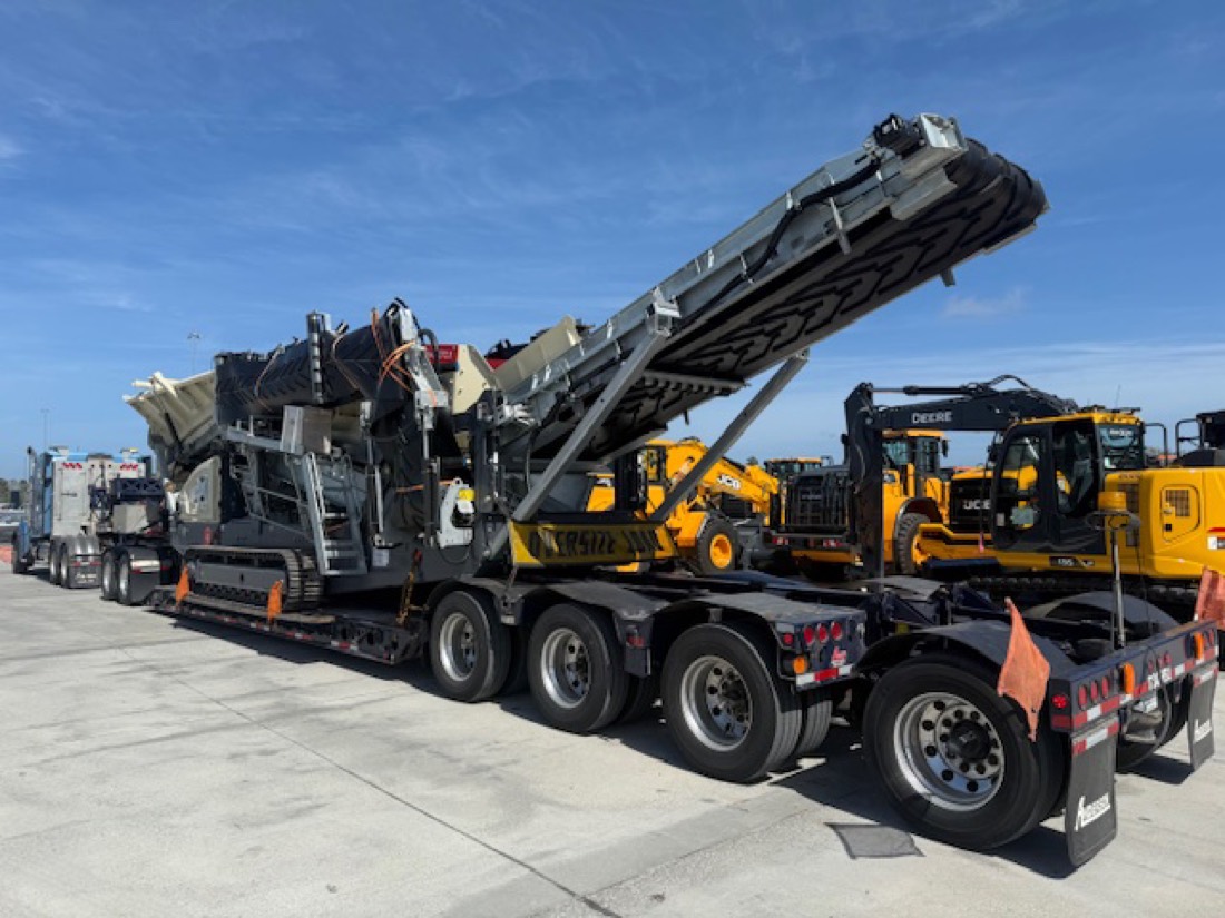 Tracked mobile crusher with raised radial stacker on Anderson lowboy at equipment yard