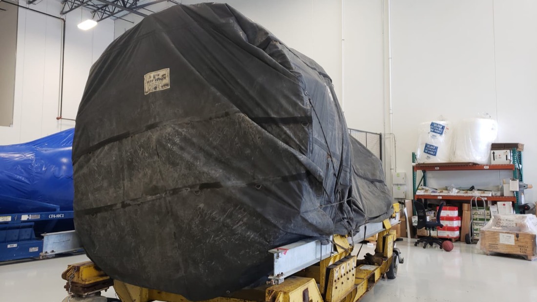Tarp-wrapped jet engine on yellow engine stand inside aerospace MRO facility (MRP Repair)
