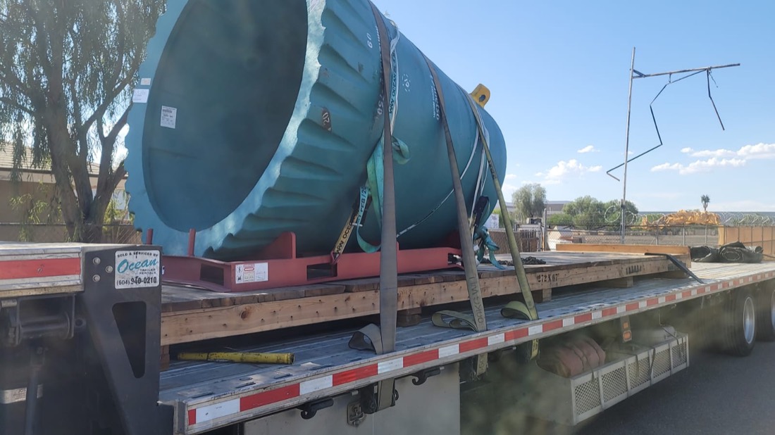 Large teal heat exchanger / vessel head on red transport skid on flatbed