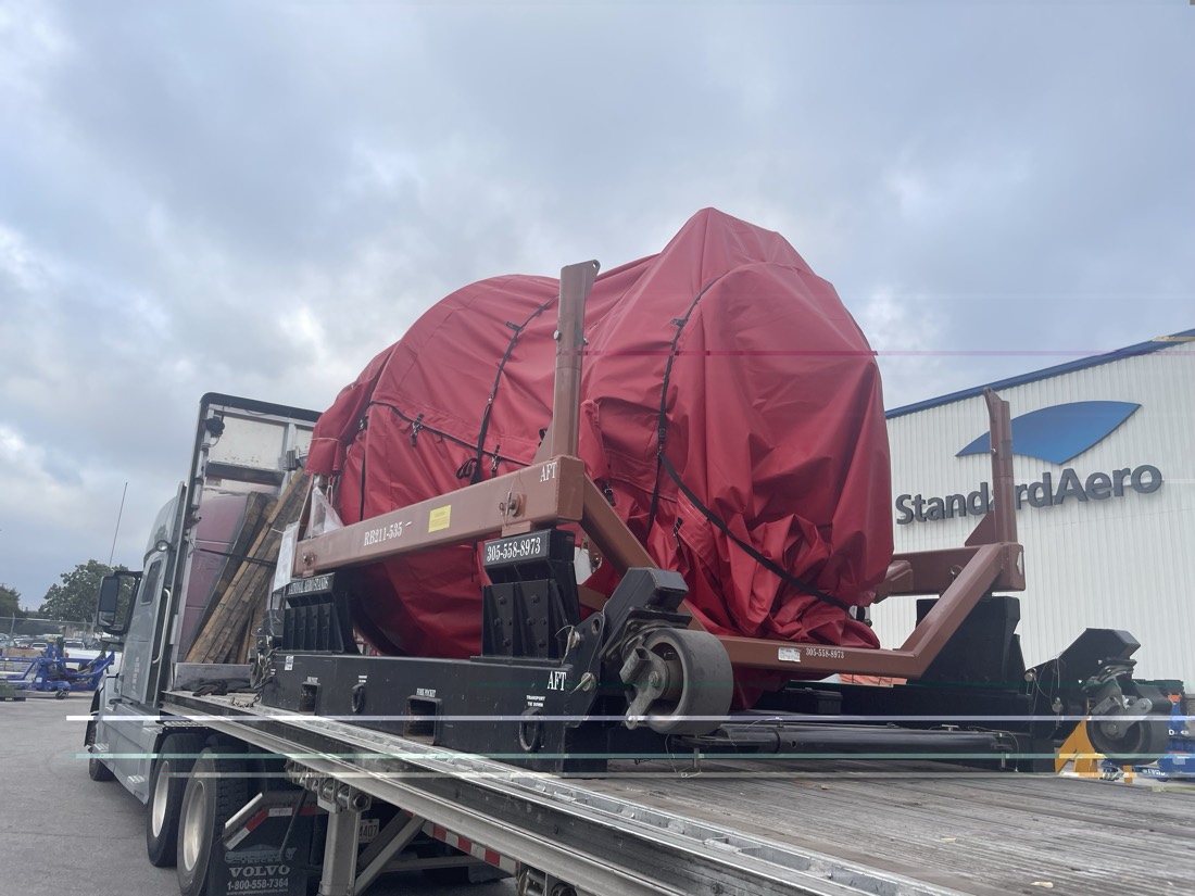 Same red-tarped RB211-535 engine on transport stand on Volvo flatbed at StandardAero (side view)