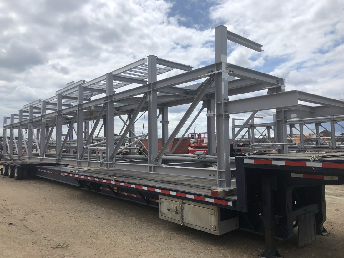 Same structural steel building skeleton on flatbed — end view at fab yard