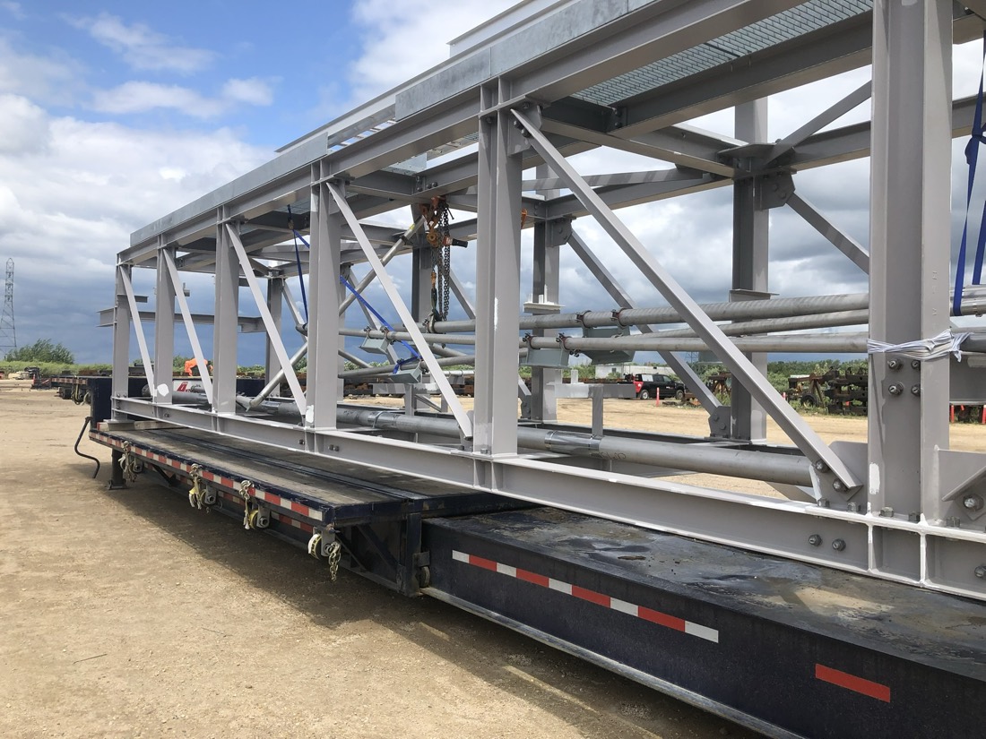 Long structural steel truss / catwalk-frame section on lowboy at fab yard