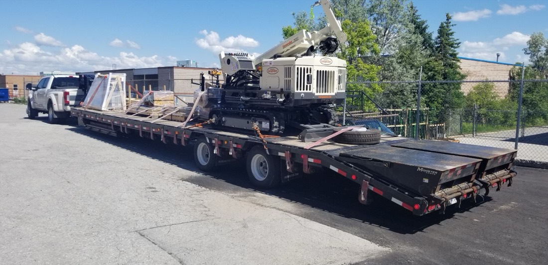 Horizontal directional drilling (HDD) rig on step-deck pulled by white pickup