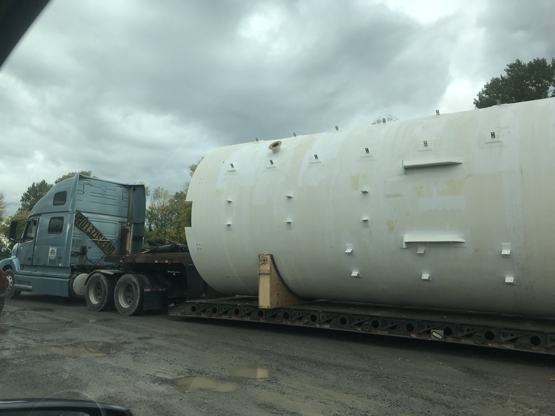 Large white fiberglass storage tank on lowboy pulled by blue Volvo