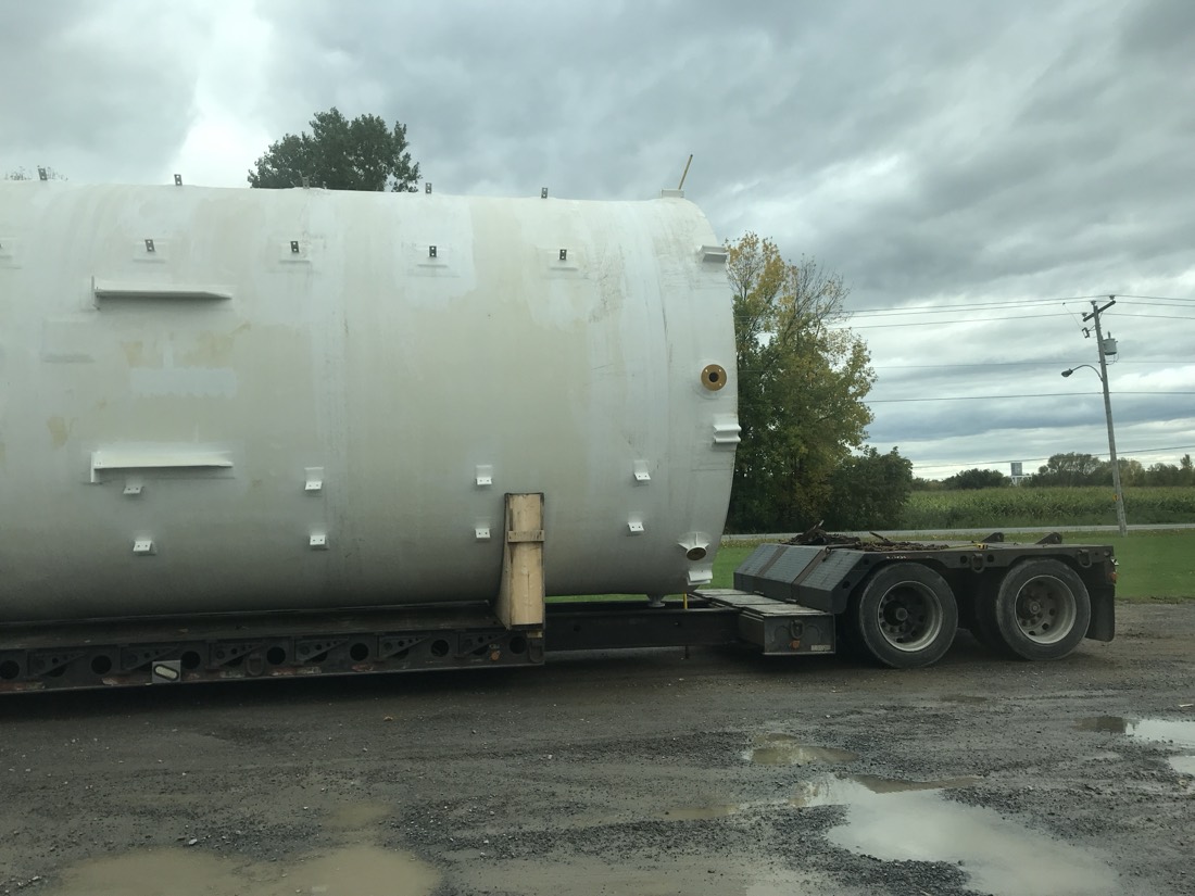 Same white fiberglass storage tank on lowboy — closer side view